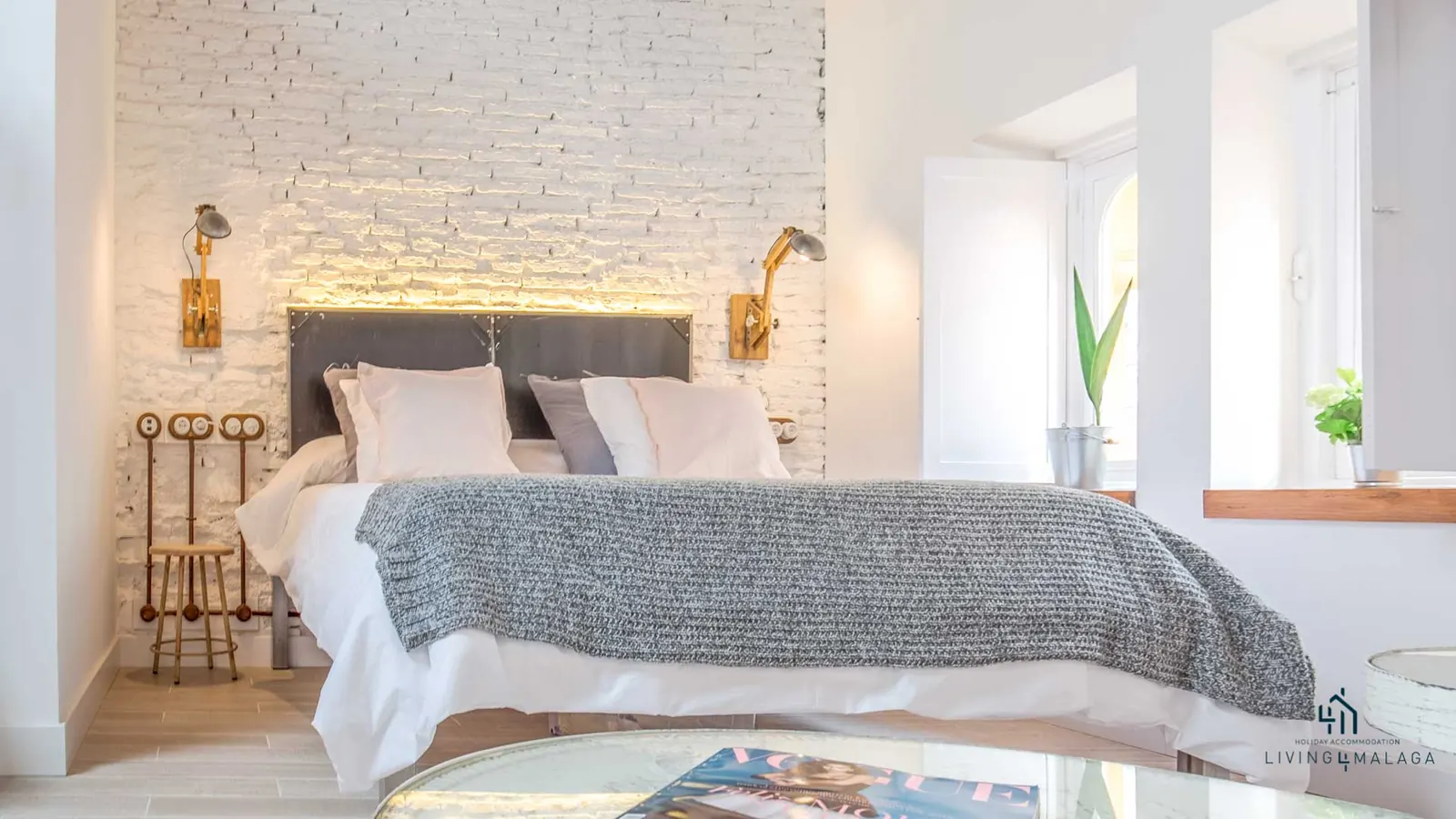 Cama con cabecero oscuro sobre pared de ladrillo encalado
